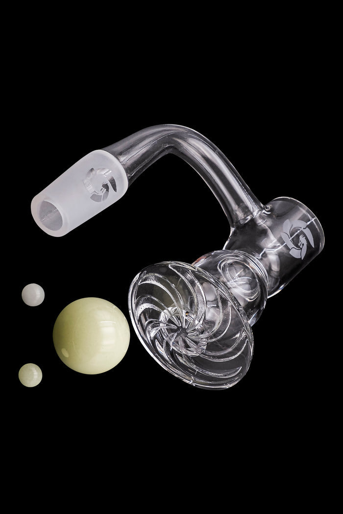 Clear glass dab rig with swirling design and accompanying small glass marbles, isolated on a black background.
