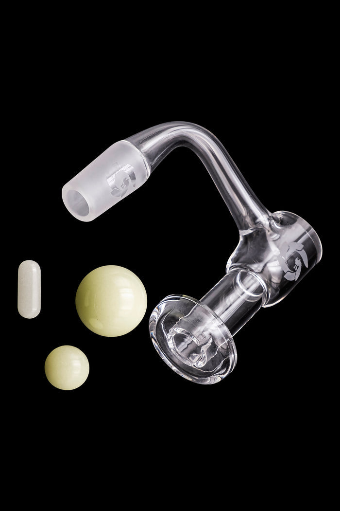 Clear glass dab rig with quartz insert and cannabis concentrates floating nearby on a black background.