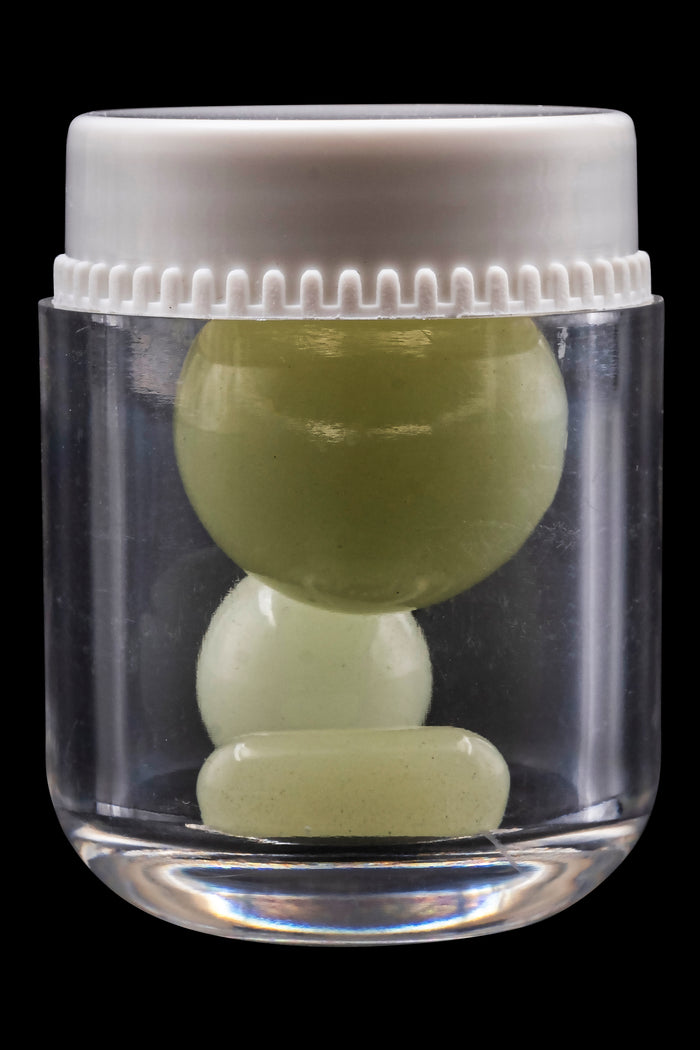 Clear glass jar containing three green cannabis capsules against a black background.