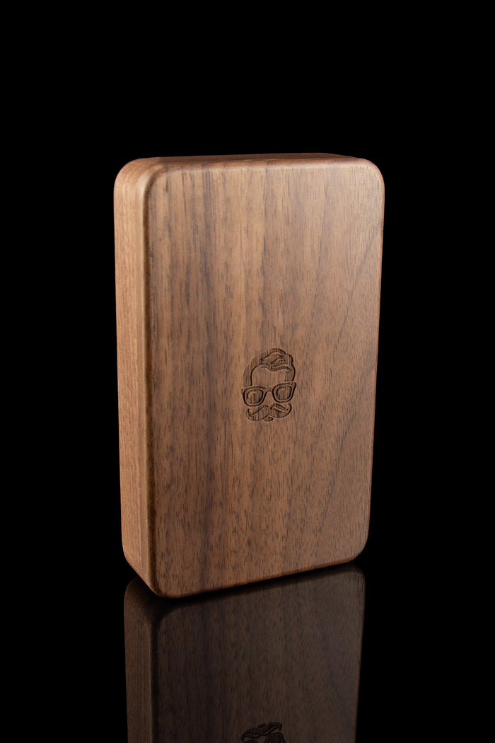 Wooden cannabis storage box with engraved skull design, displayed on a reflective surface.