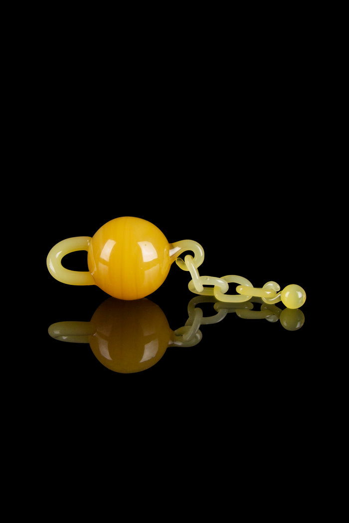 Yellow glass cannabis water pipe with spherical bubbler and intricate design, reflecting on a black surface.