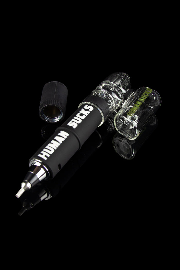 Black electronic dab rig with glass bubbler, displaying “HUMAN SUCKS” text, against a dark background.