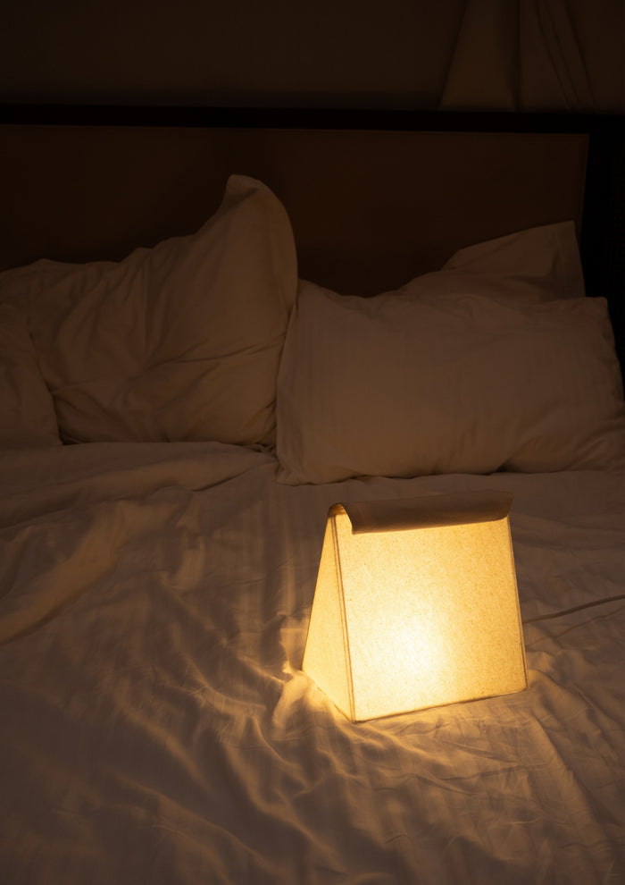 Small glowing lamp placed on a bed with white pillows and sheets.