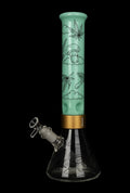Studio-lit vertical view of the Prism Halo Mint Sky High Modular Bong showing a mint green straight tube with black mushroom and leaf illustrations above a clear beaker base and gold modular band