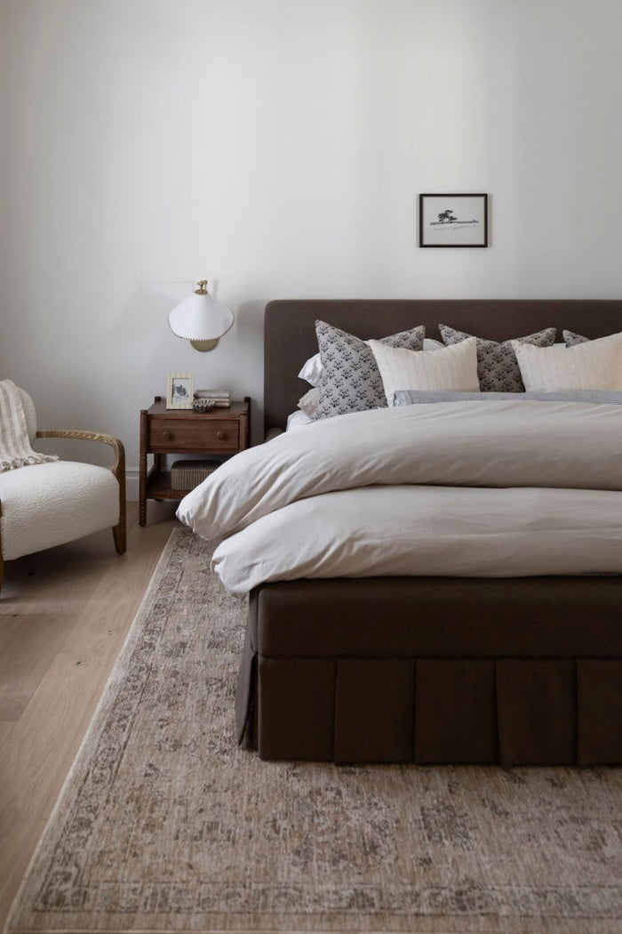 Willa power loomed area rug on the floor with a neatly made bed with decorative pillows in a bedroom setting.
